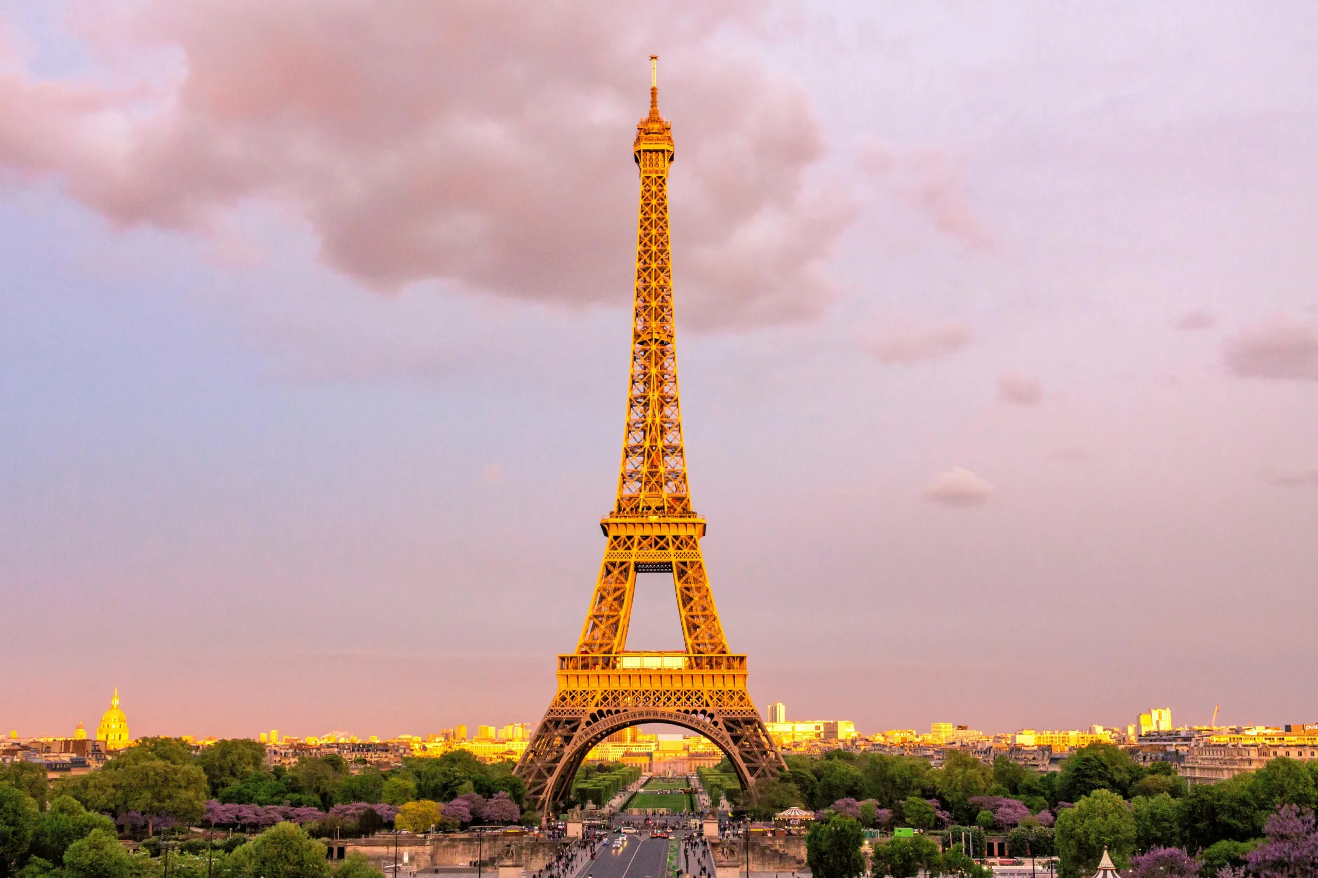 Eiffel Tower at sunset in Paris, France, with city skyline and lush greenery — iconic landmark and top travel destination in Europe.